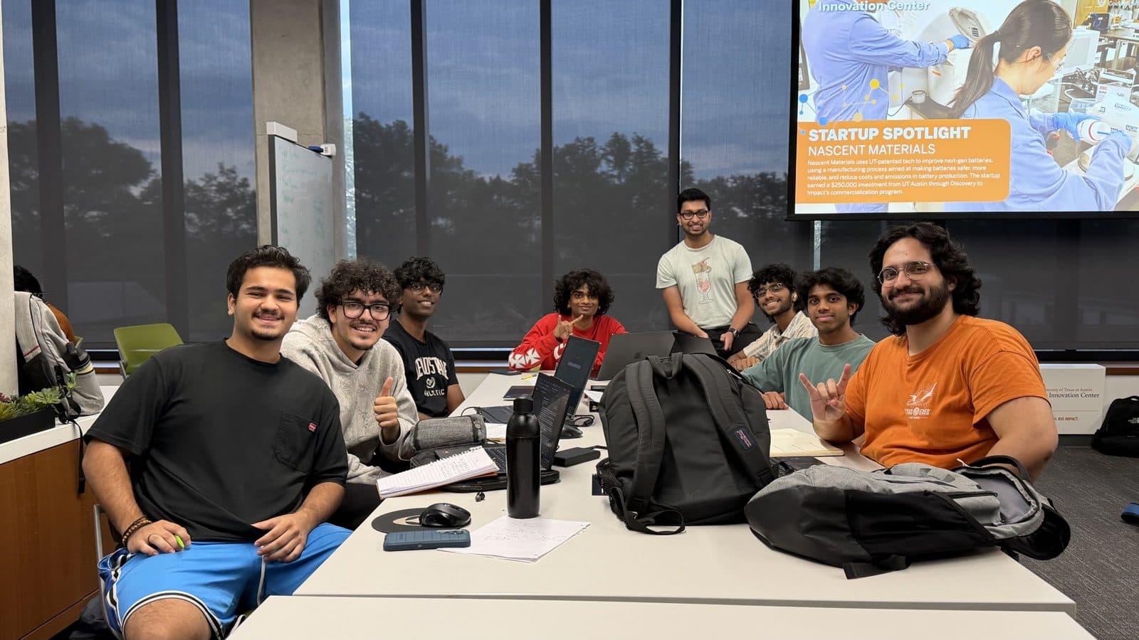 Physical design apprentices seated around a table with a startup spotlight slide on the screen behind them